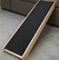 Wooden pet ramp with black non-slip surface leaning against a couch